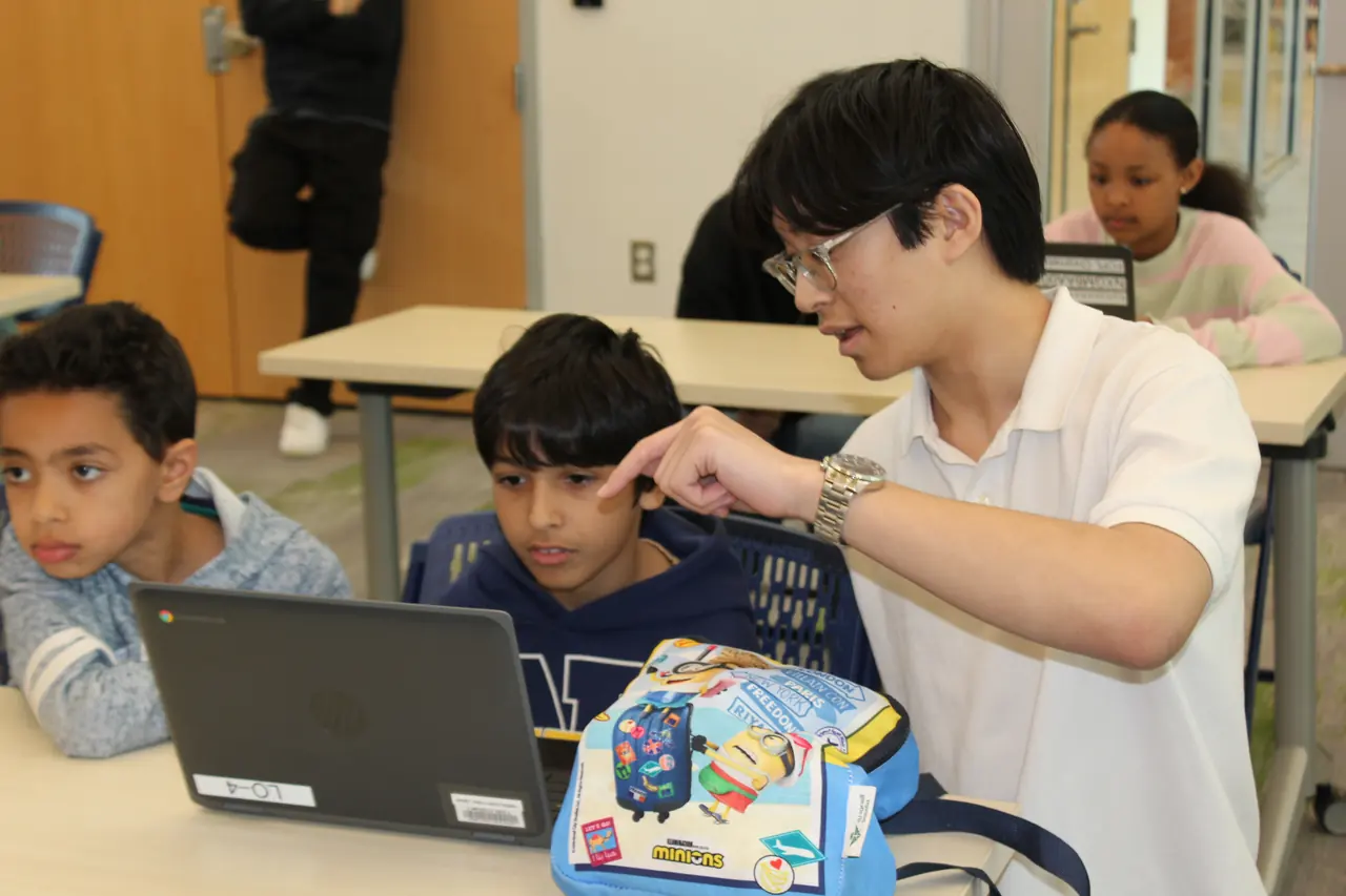 Older student mentoring younger students at a laptop